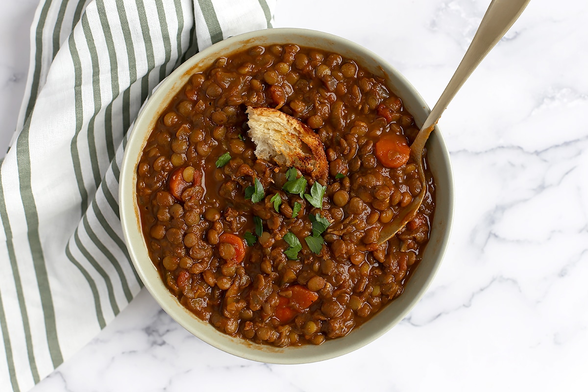 A bowl of lentil soup topped with a crust of bread and fresh chopped parsley.