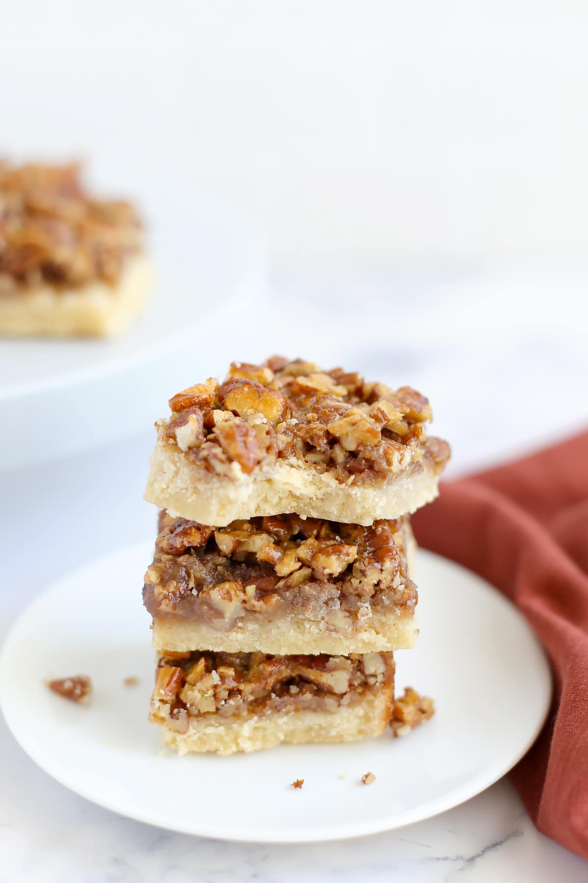 A stack of pecan pie bar squares on a small white serving plate.