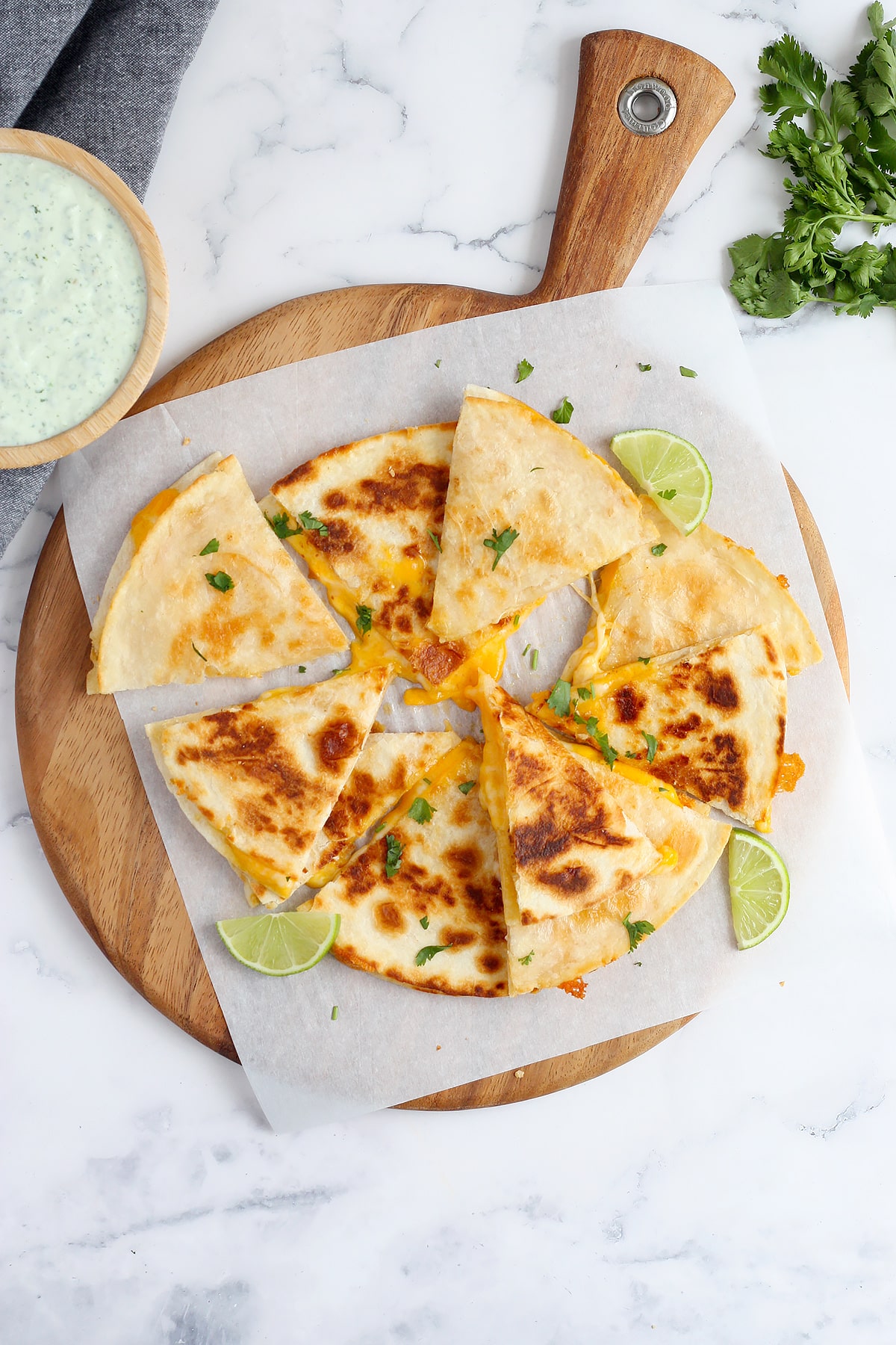 An overhead s،t of ،memade cheese quesadillas on flour tortillas and topped with c،pped cilantro and lime slices.