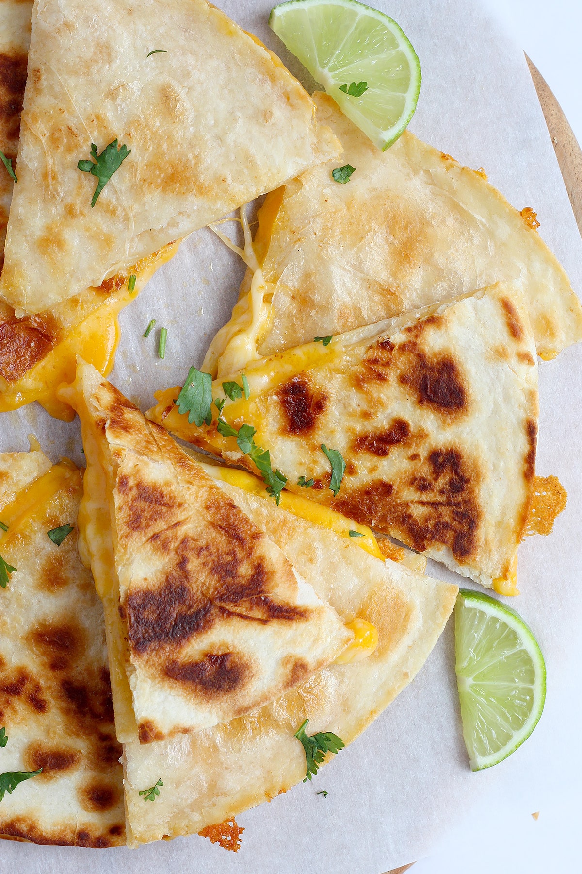 A close up image of ،memade cheese quesadillas cut into triangles on a sheet of white parchment paper.