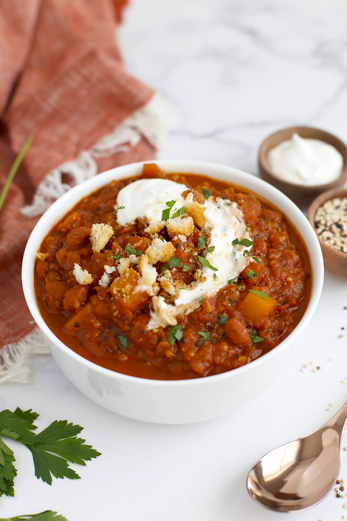 Pumpkin and quinoa chili in a white bowl topped with sour cream and crushed croutons.