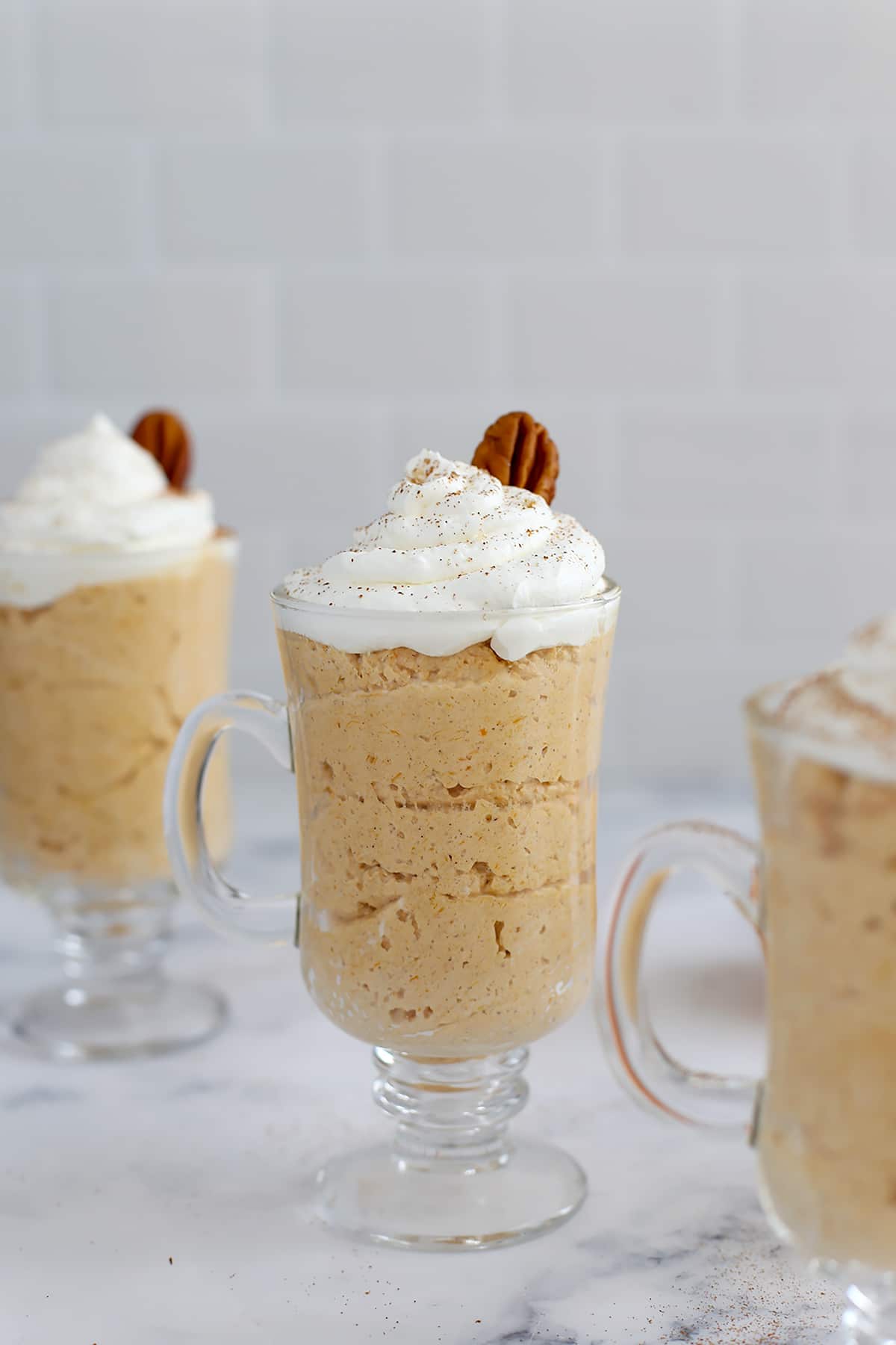 A glass serving mug filled with pumpkin mousse and topped with whipped cream and a pecan.