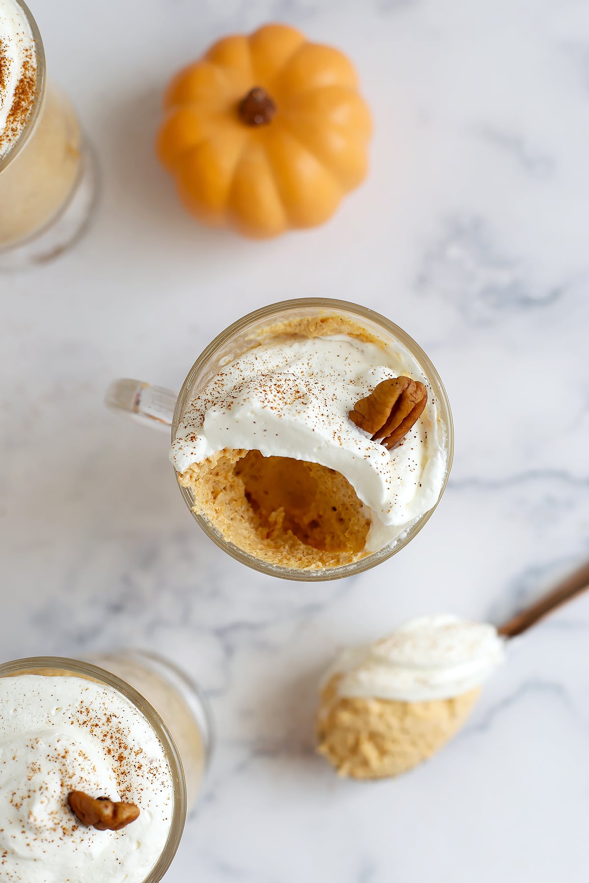 An overhead shot of pumpkin mousse in a glass mug topped with whipped cream and a pecan with a big spoonful scooped out.