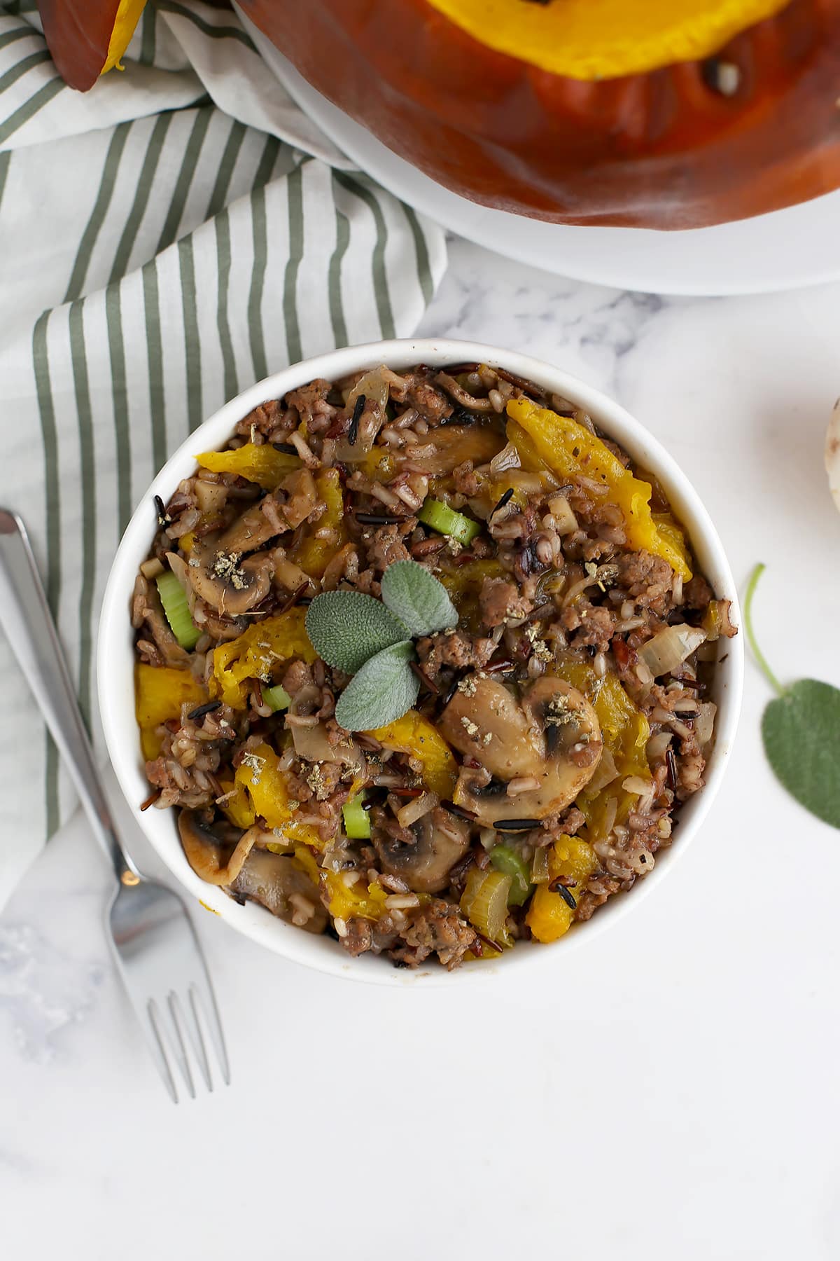 Rice, ground beef, mushrooms and baked pumpkin in a serving bowl with a striped linen in the background.