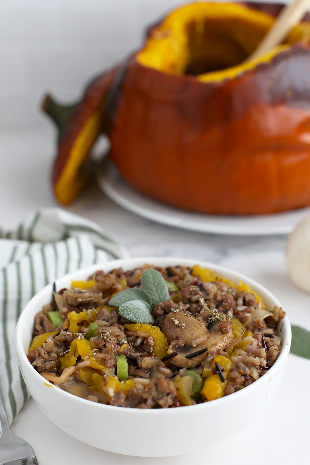 Dinner in a pumpkin, scooped into a white serving bowl and topped with fresh sage.