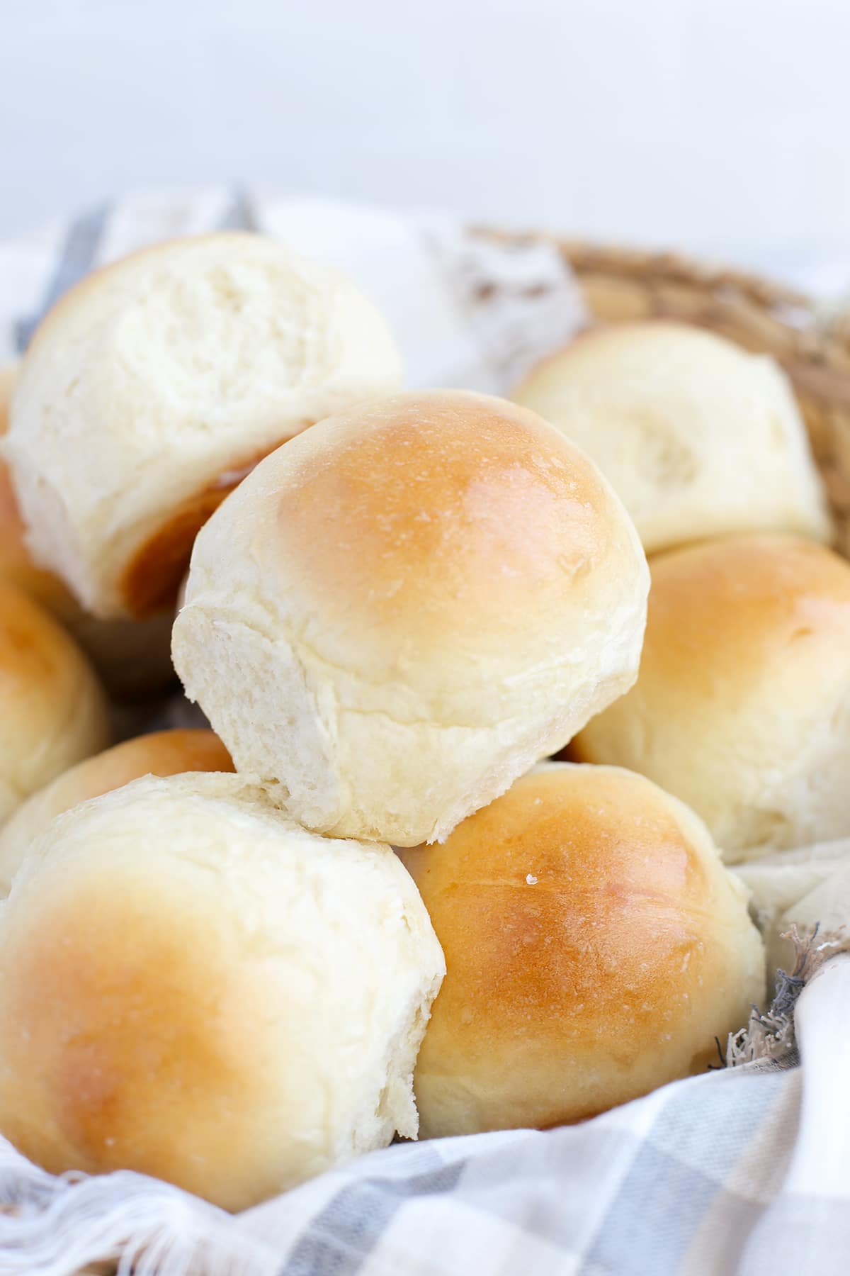 A basket  with a plaid linen full of homemade dinner rolls with a shiny brown top.