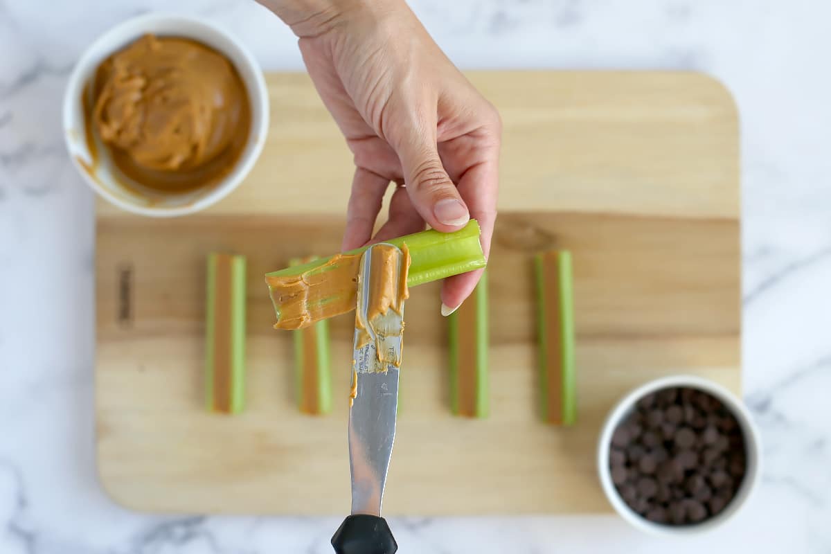 Someone spreading peanut butter on a celery stick.