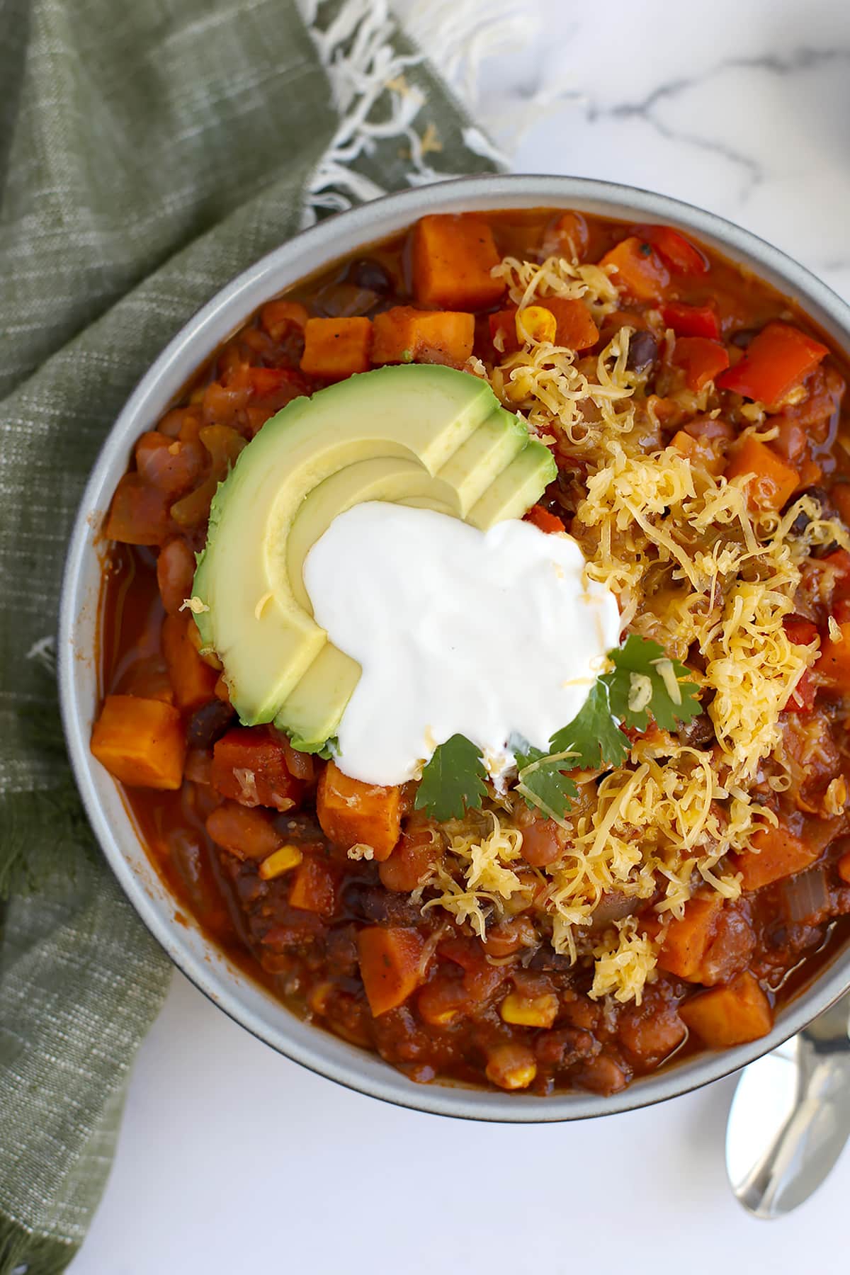 veggie chili in a serving bowl with shredded cheese and sour cream with a green linen