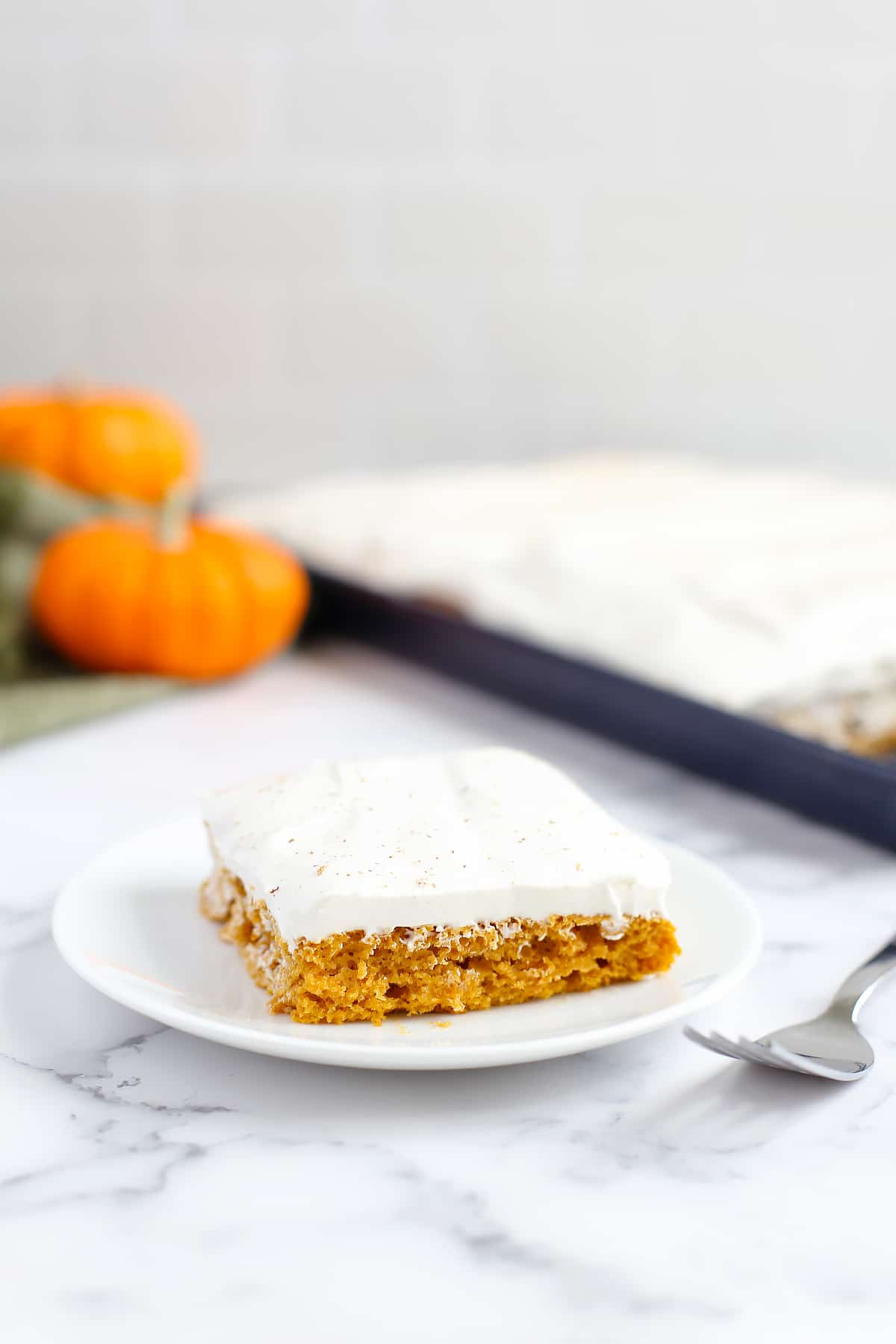 Pumpkin cake with whipped topping garnished with nutmeg with a green linen and a small pumpkin in the background.