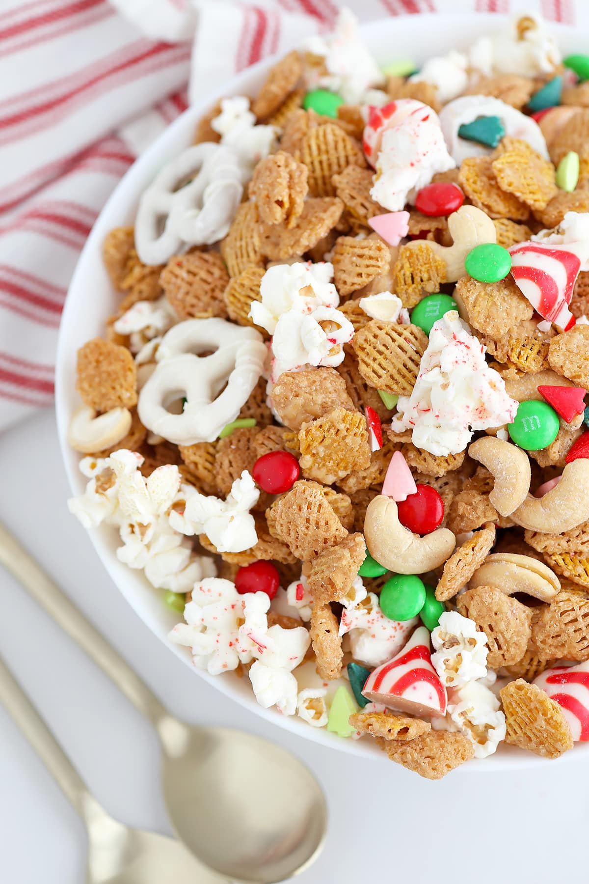 A large white serving bowl filled with a holiday snack mix and toped with festive sprinkles.