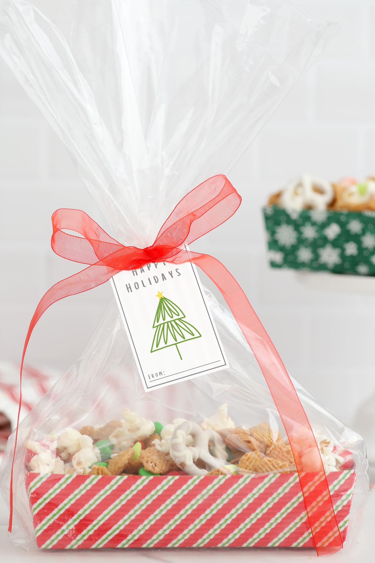 Christmas Snack Mix in a striped gifting box tied with a ribbon and a printable gift tag.