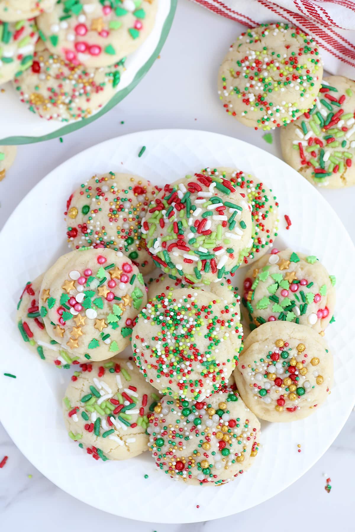 A plate of sugar cookies topped with Christmas sprinkles piled on a white serving plate.