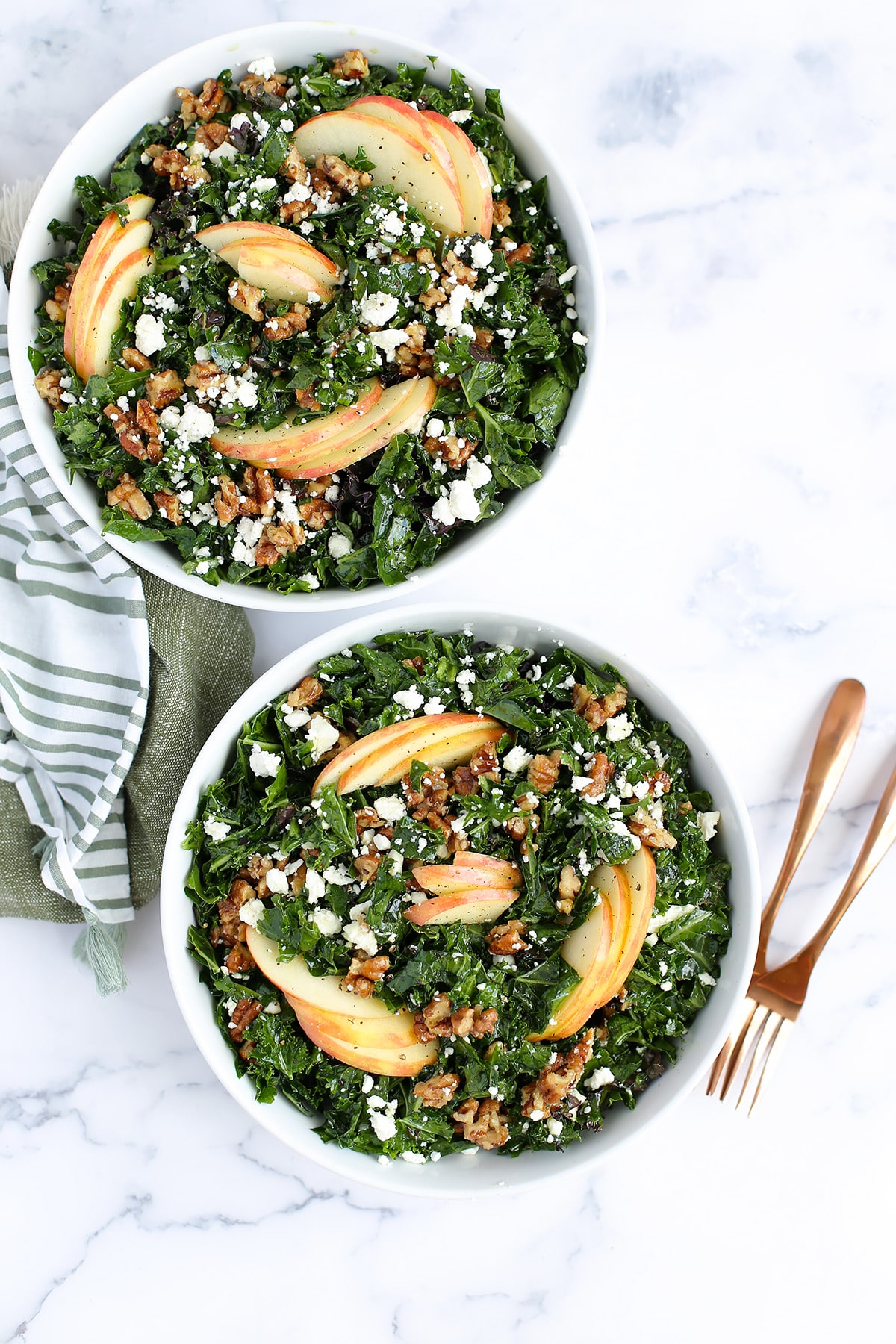 kale salad with apples, feta and pecans with copper forks and linens