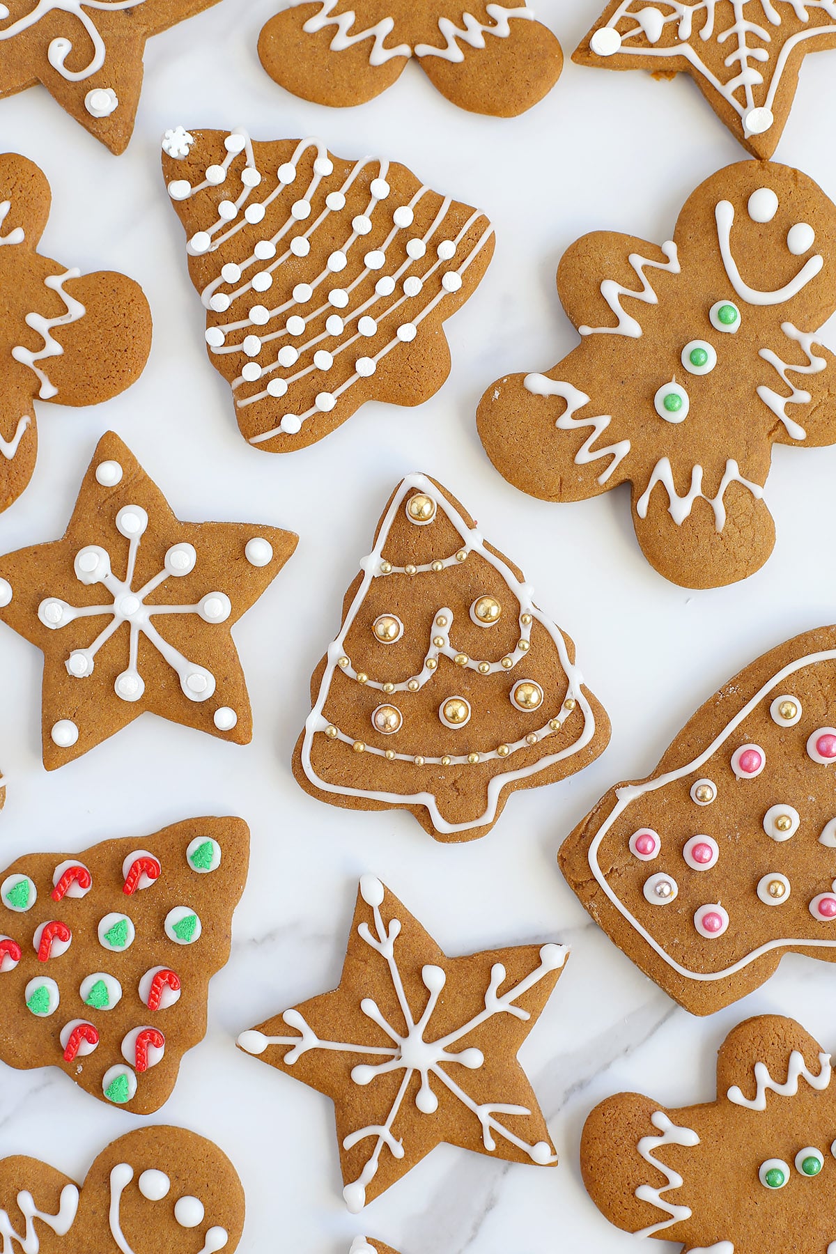 Decorated gingerbread cookies shaped like christmas trees, stars, and gingerbread men decorated with icing and sprinkles on a marble countertop.