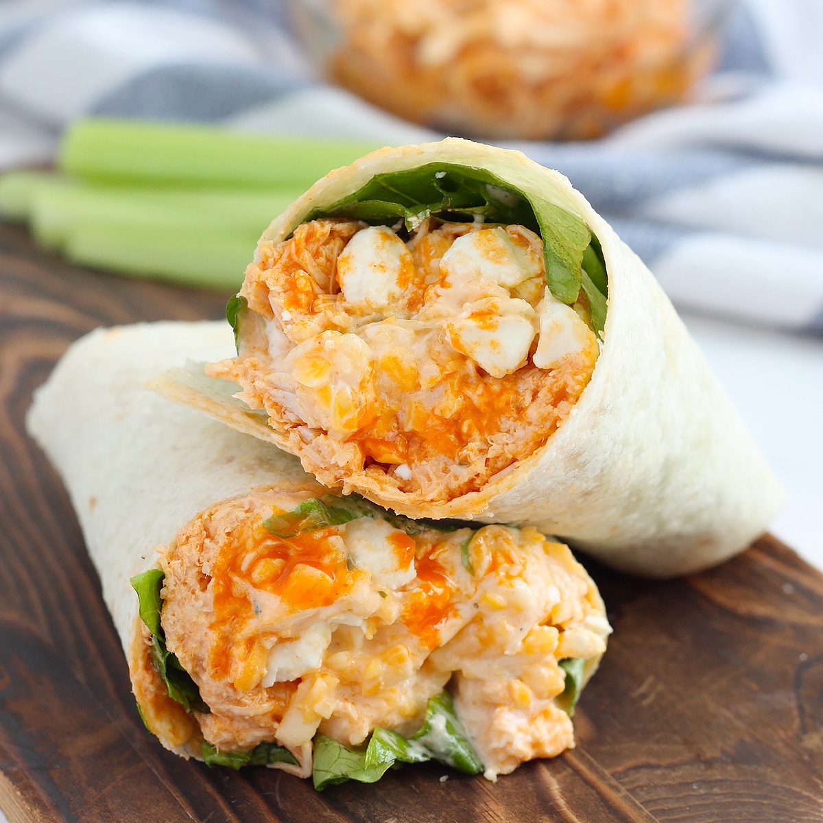 Buffalo chicken wraps in a soft flour tortilla stacked on a wooden cutting board.