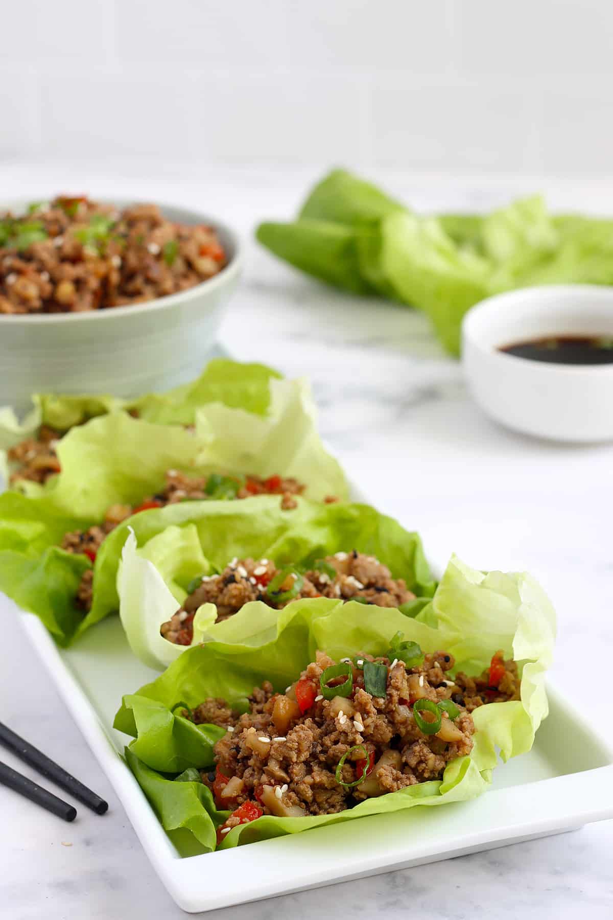 asian lettuce wraps on a long white serving platter with a bowl of soy sauce for dipping