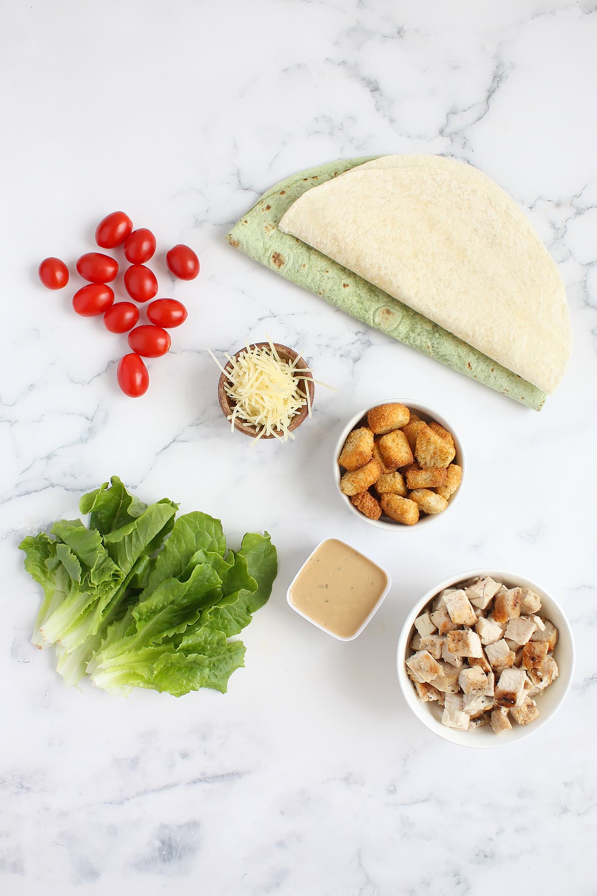 ingredients you need to make chicken caesar wraps on a marble countertop