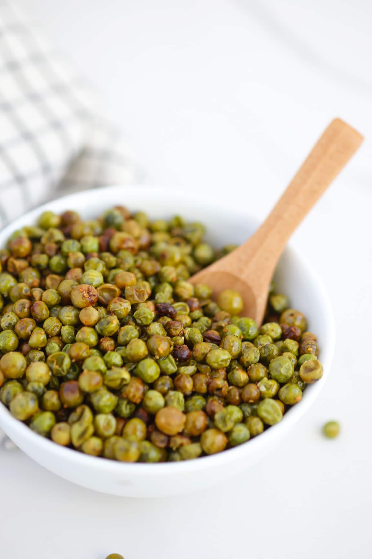 roasted peas in a serving bowl with a wooden spoon