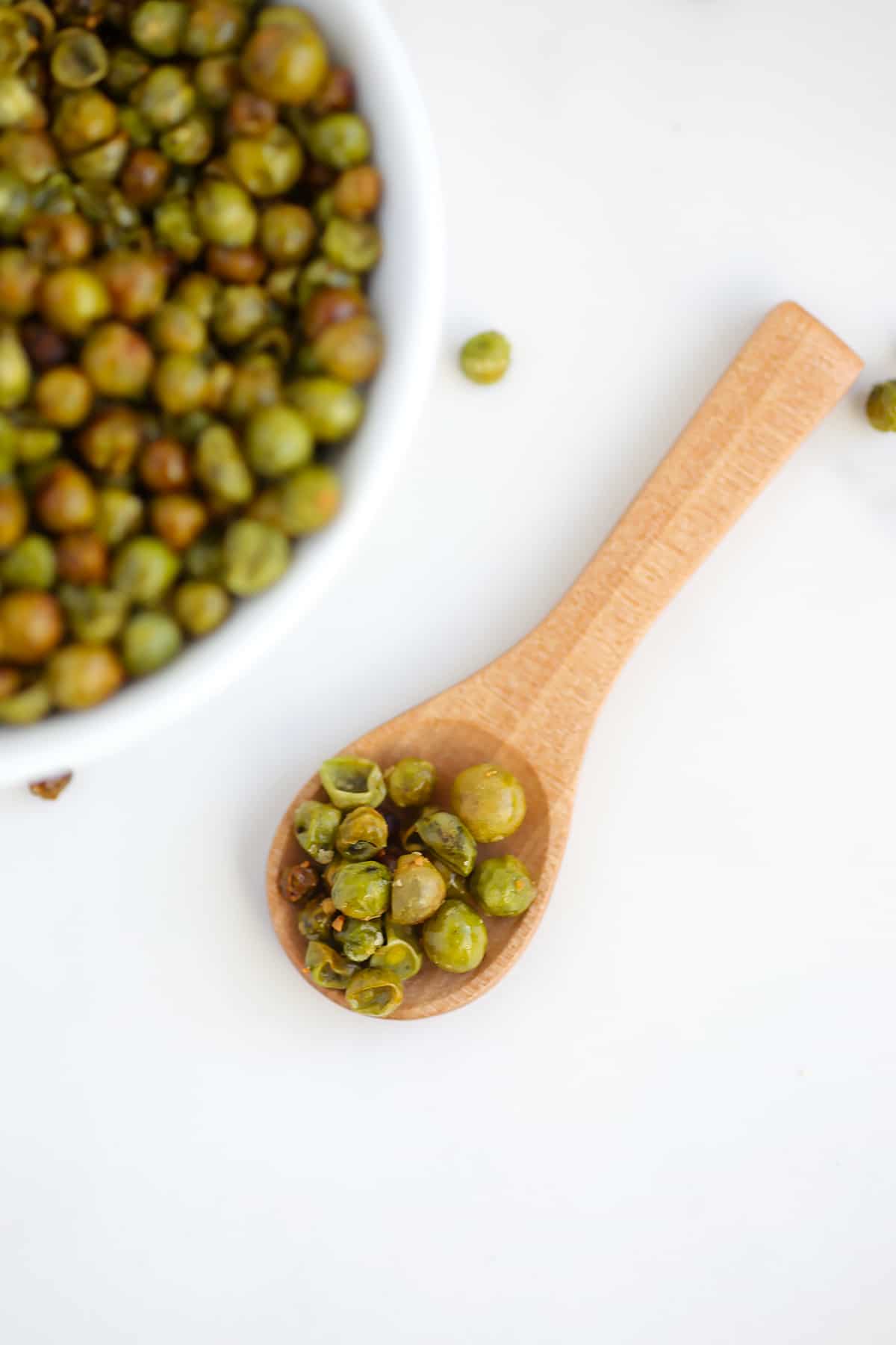roasted peas on a small wooden spoon with a bowl of peas in the background