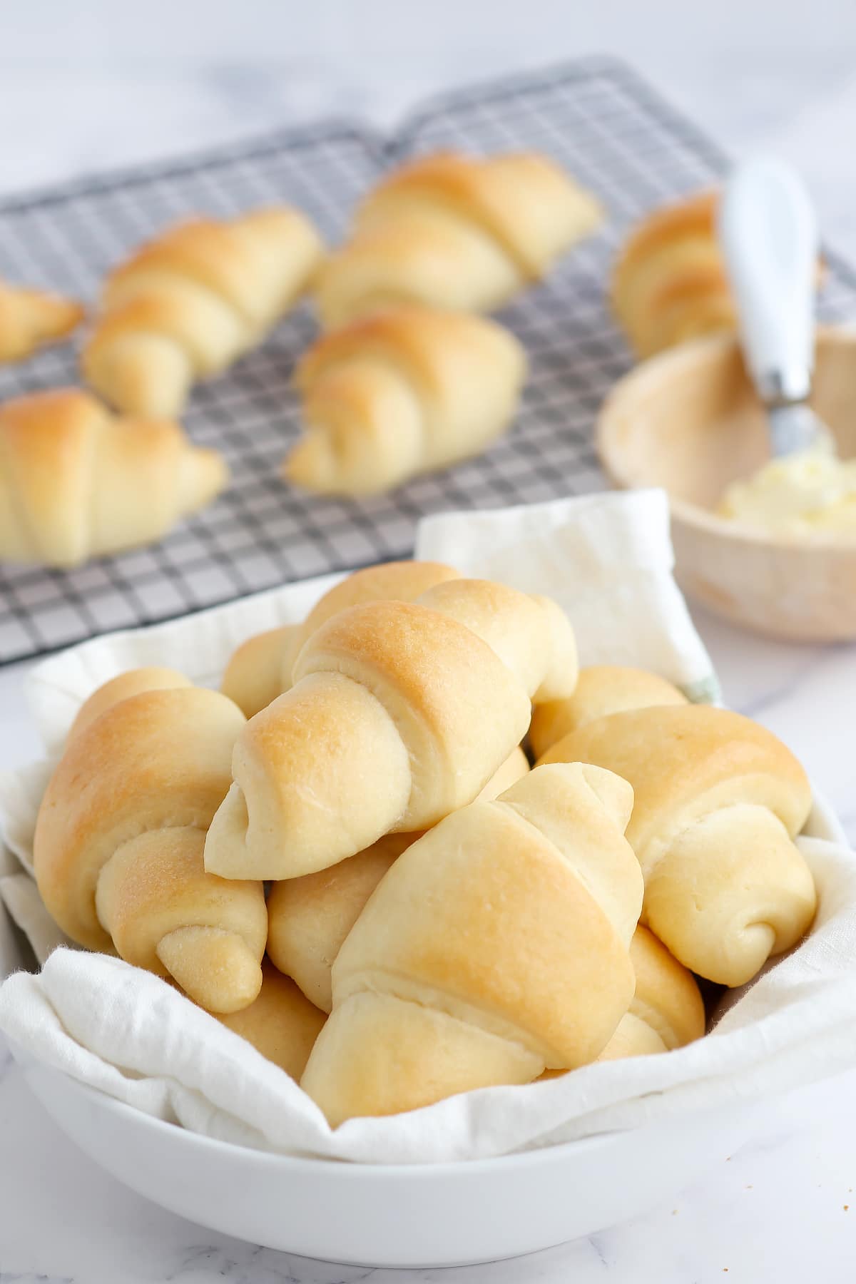 a close up picture of fluffy homemade crescent rolls piled into a serving bowl with a white linen