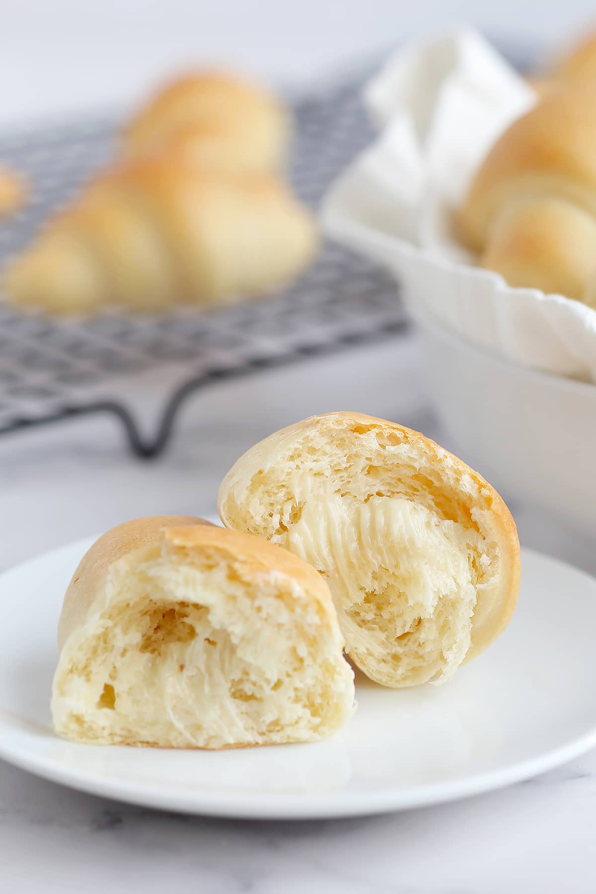 a fluffy homemade crescent roll torn in half and set on a small plate and spread with butter
