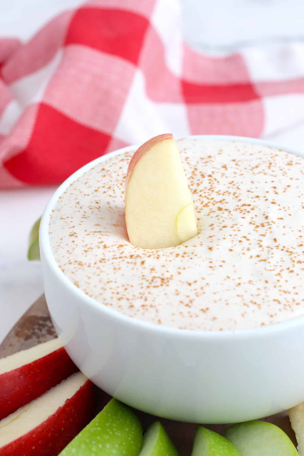 an apple slice dipped into a bowl of yogurt fruit dip with cinnamon in a white serving bowl