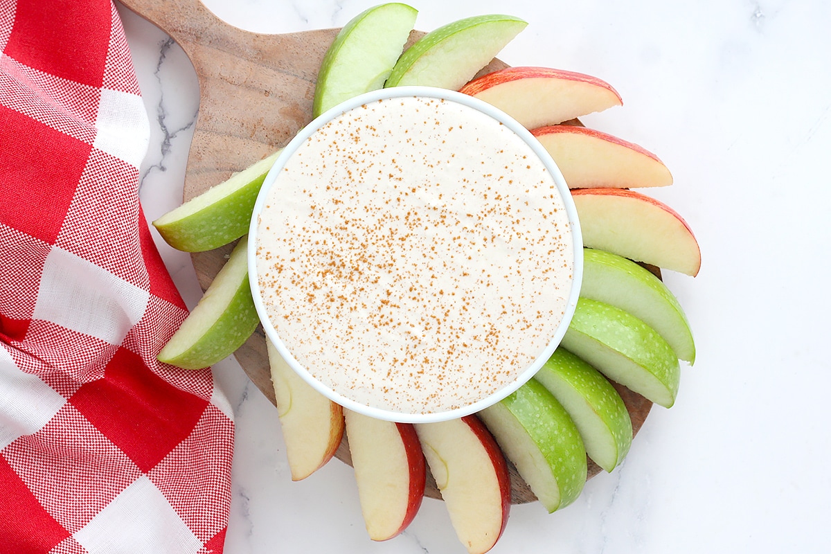 healthy yogurt fruit di[p topped with cinnamon anbd served with red and green apple slices