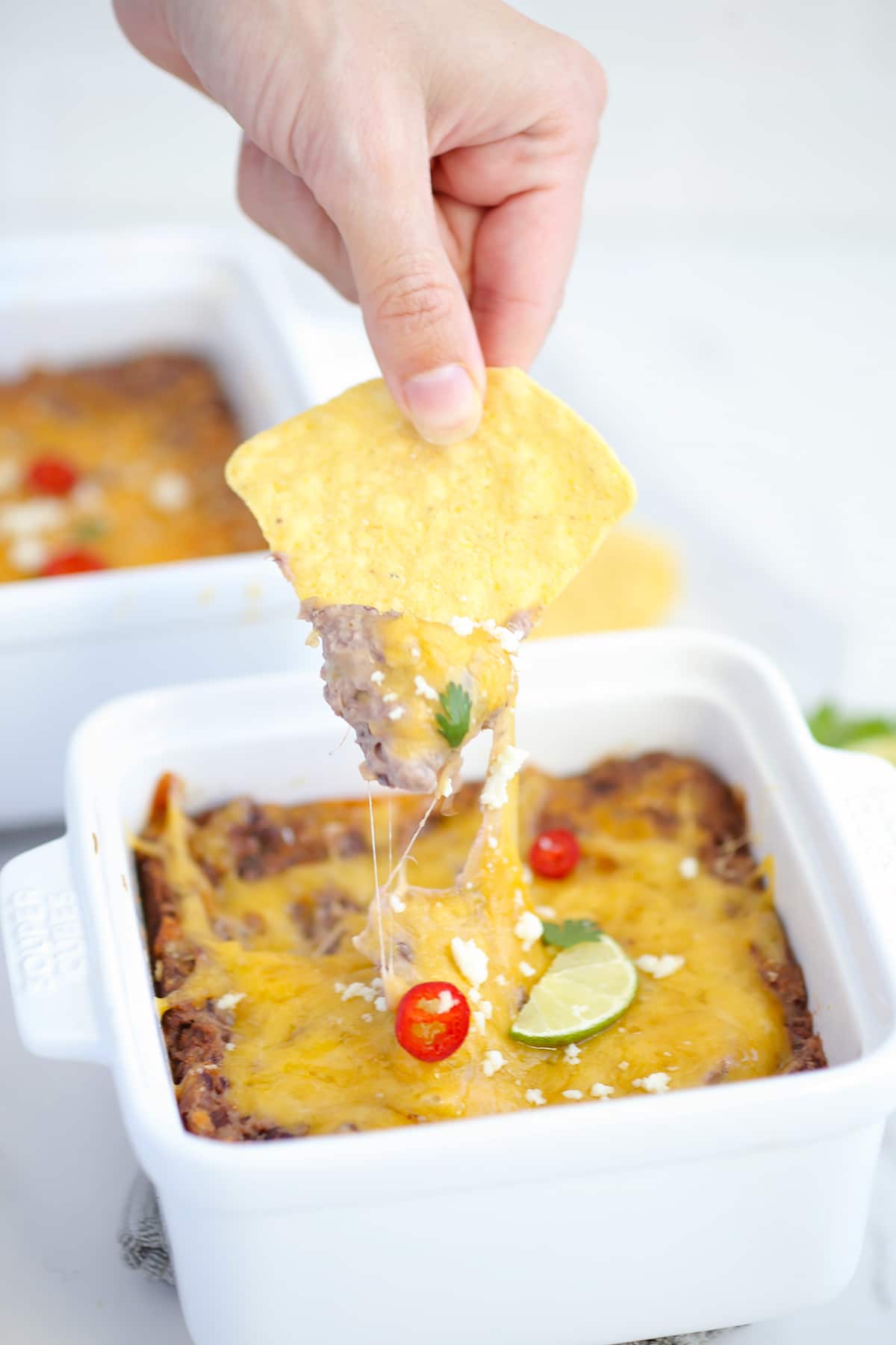 black bean dip being scooped out with a tortilla chip with a string of melted cheese