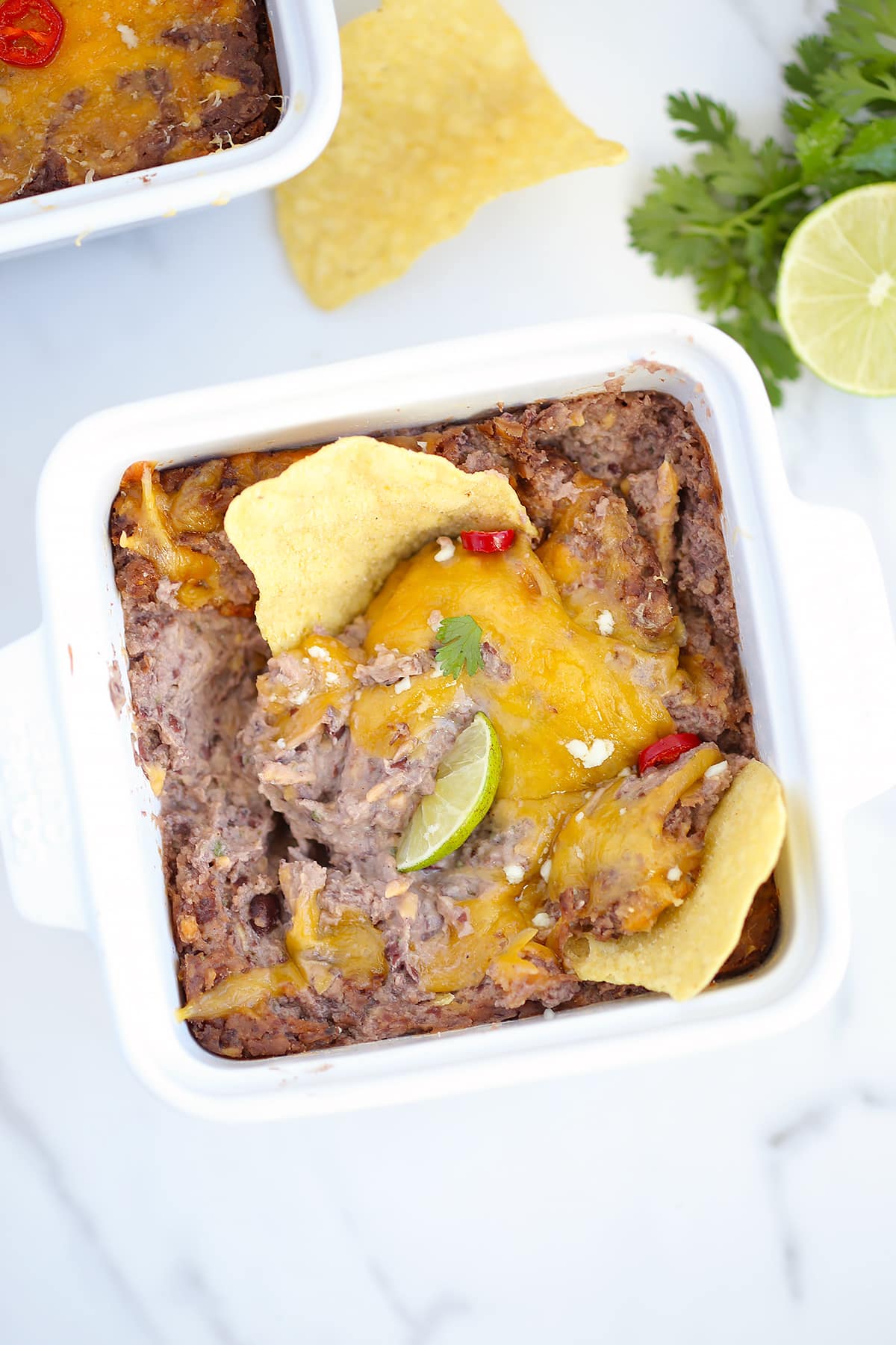 black bean dip with melted cheese, fresh lime and tortilla chips in a white baking dish