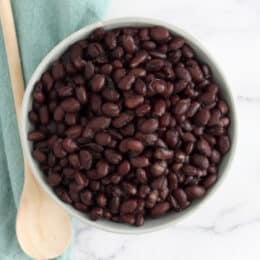 a bowl of cooked black beans with a wooden spoon next to them