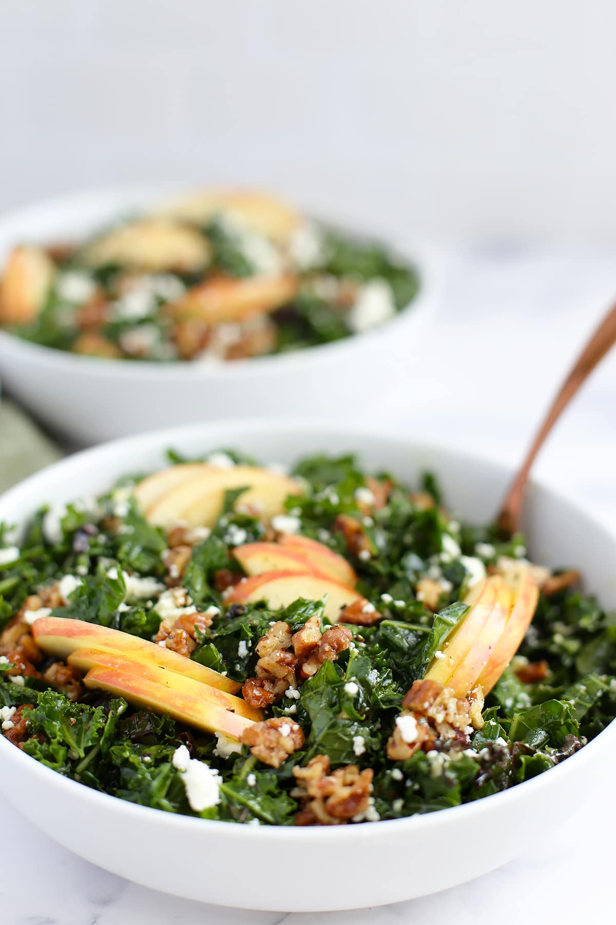 a close up image of massaged kale salad with apple slices in a large serving bowl