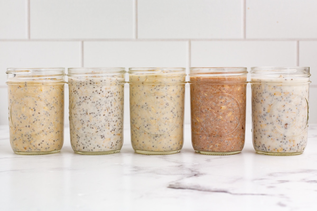a line of jars filled with different flavors of overnight oats on a marble countertop