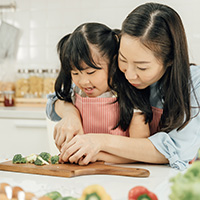 Mother helping daughter learn to cut broccoli