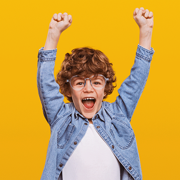 Boy with red curly hair and glasses in denim shirt cheering with arms lifted above his head