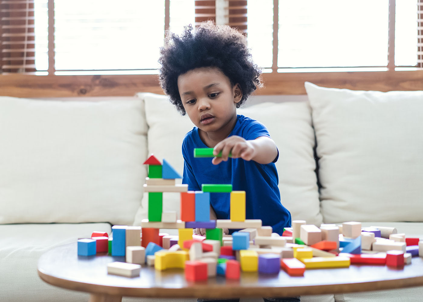 Little boy building a tower with colorful wood blocks on a coffee table