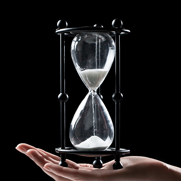 Hourglass with sand falling inside, held in the palm of a hand, against a black background