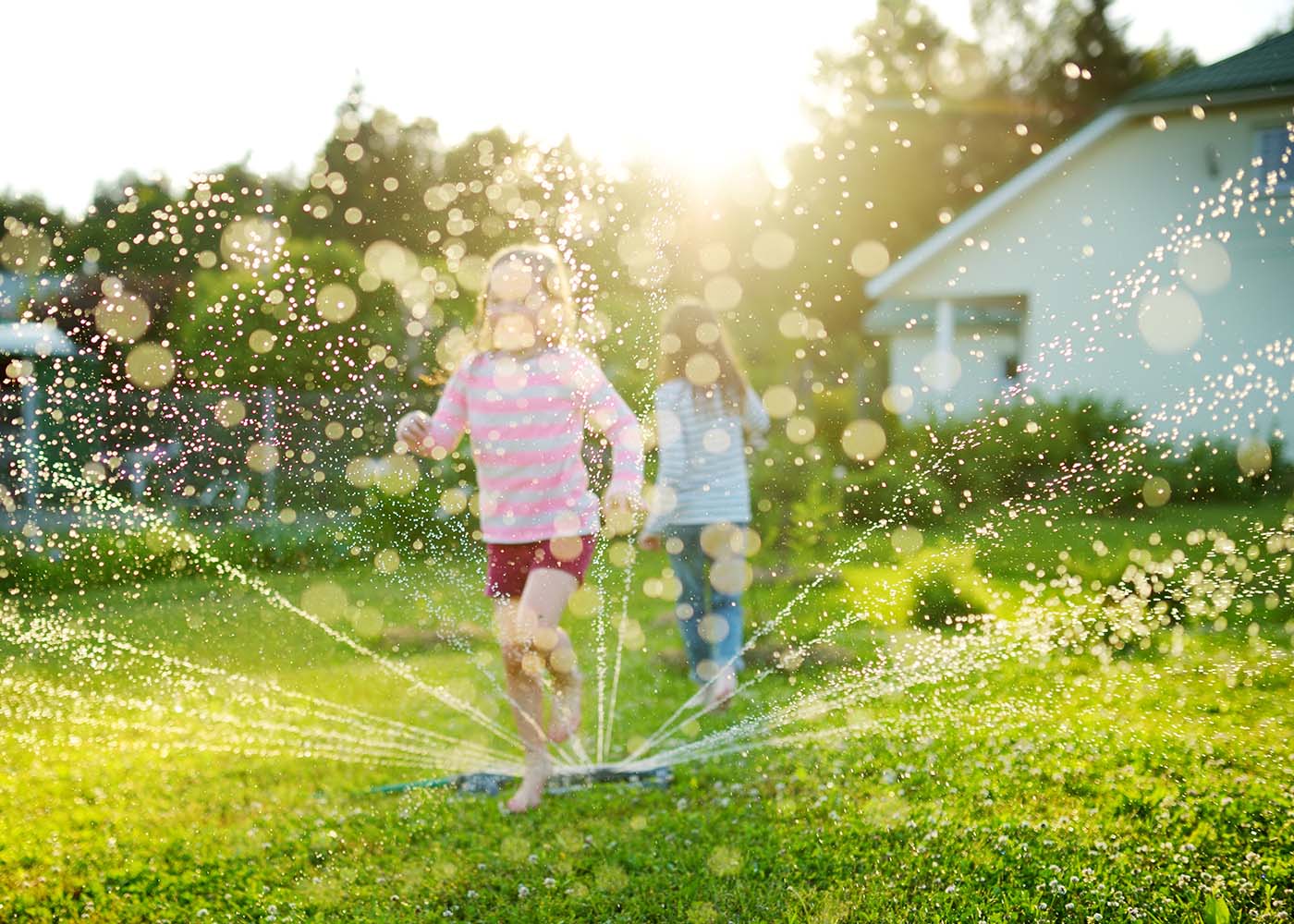 Two little girls running through a sprinkler in their backyard on a hot summer day