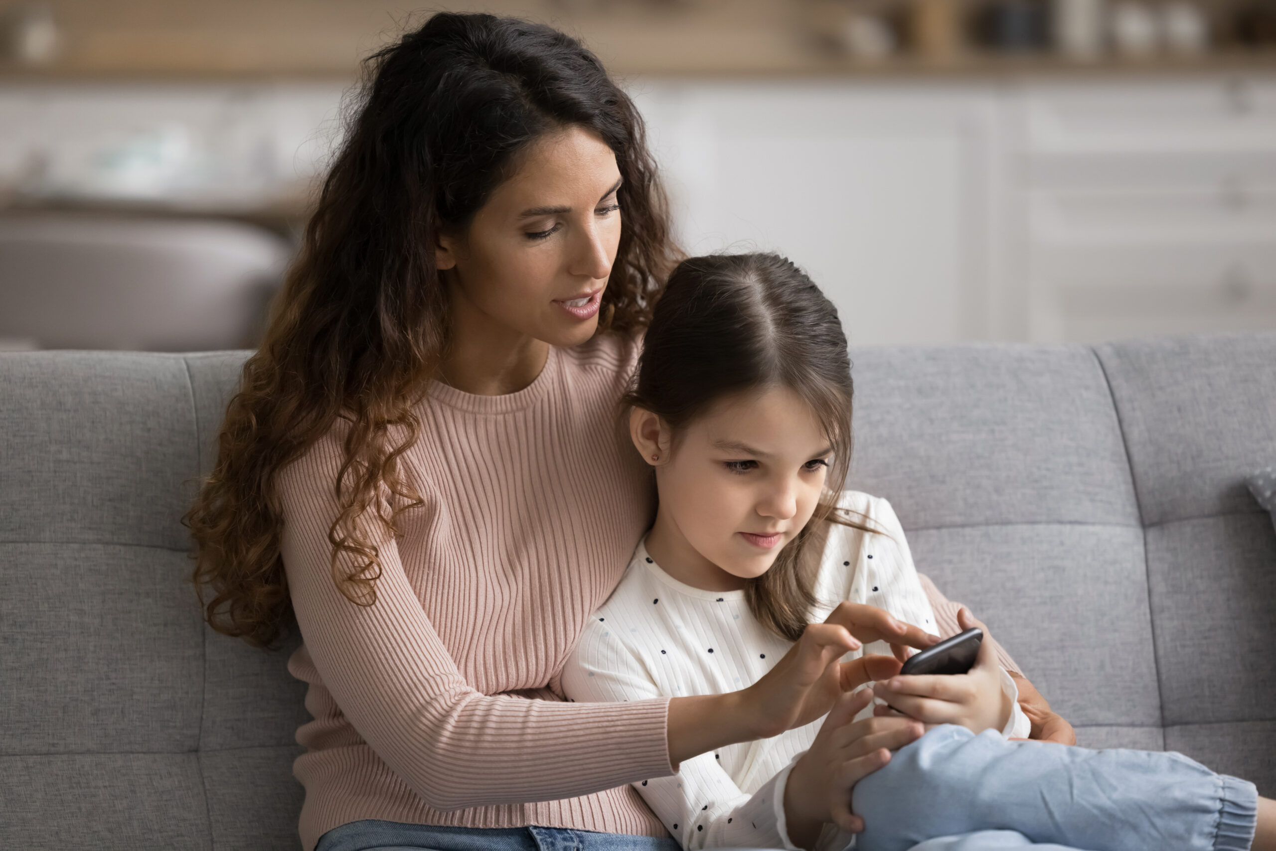 Mother and daughter sitting on a sofa holding and looking at a smartphone
