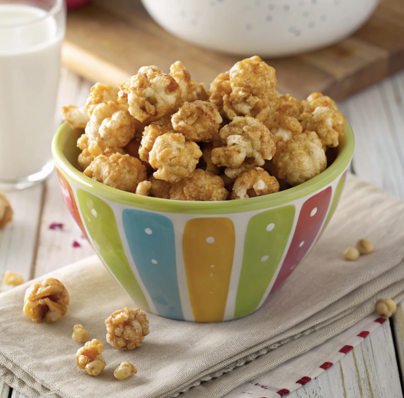 Susan's caramel corn is placed on a wooden table with a glass of milk on it.
