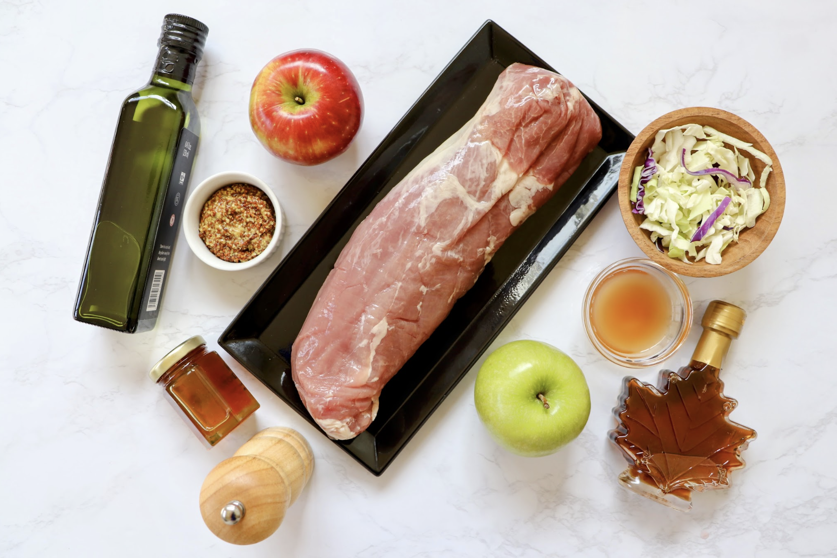 Ingredients you need to make maple pork tenderloin with apple slaw on a marble countertop.