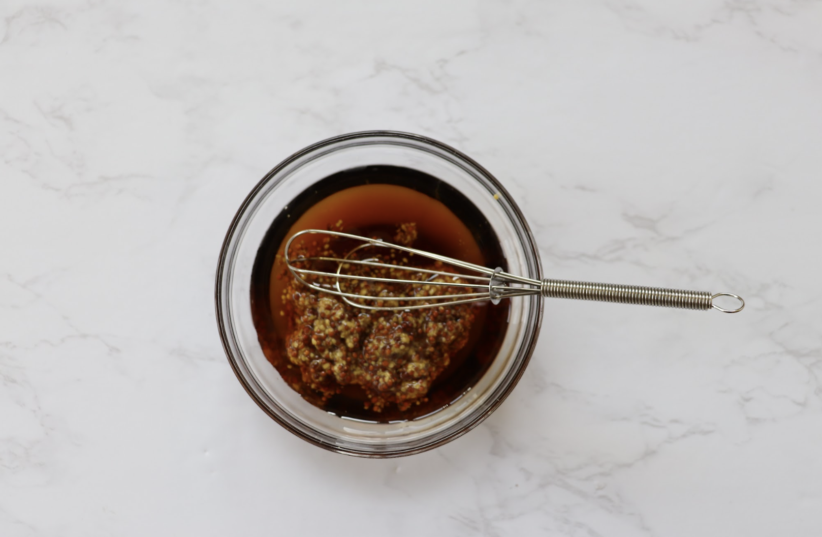 Maple glaze in a small glass bowl with a whisk.
