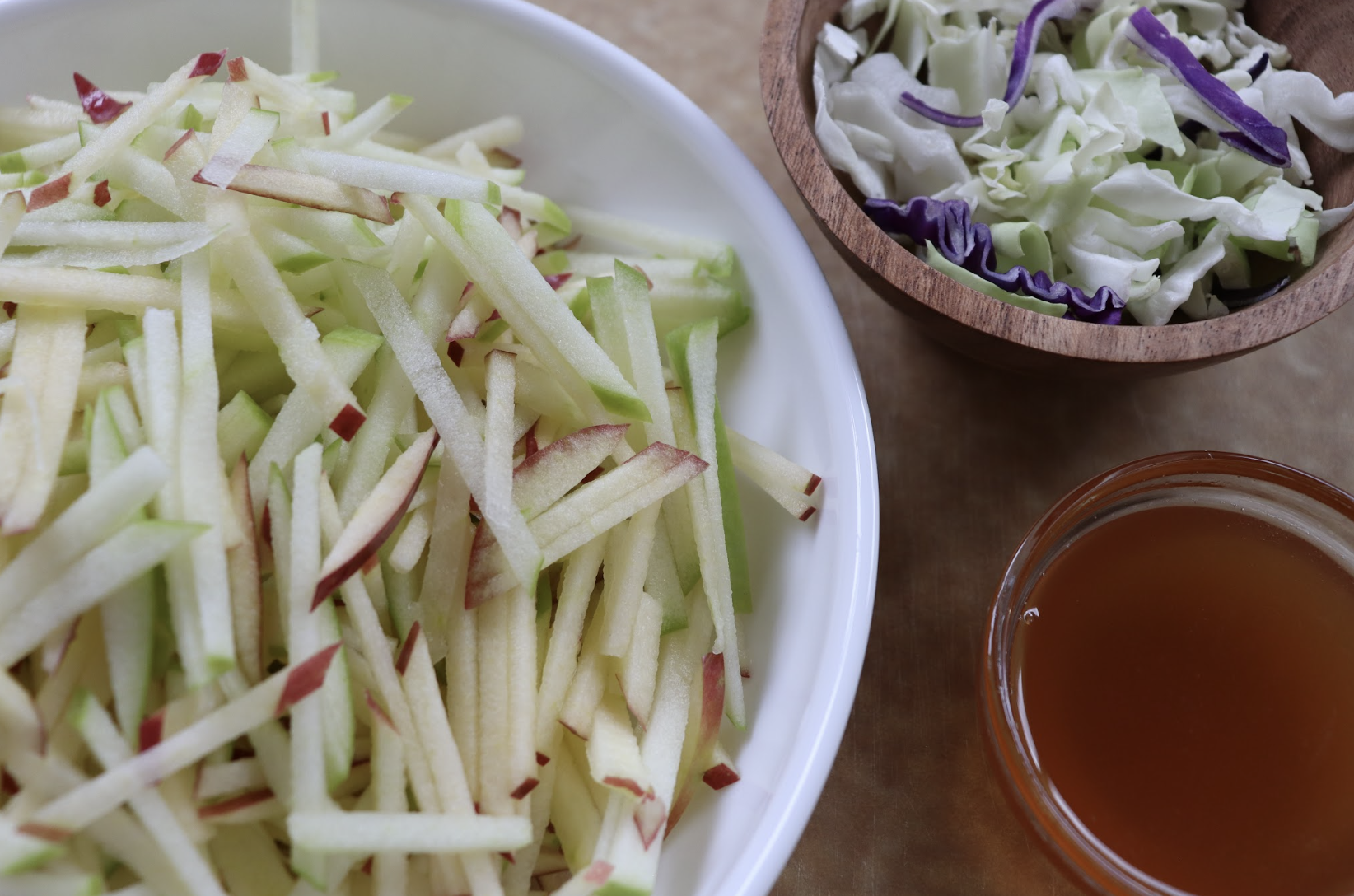 A bowl full of julienned apples and a smaller wooden bowl of shredded cabbage to make apple slaw.