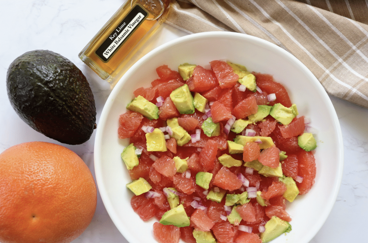 A salad made with grapefruit, avocado and red onion in a white bowl with a plaid linen in the background.
