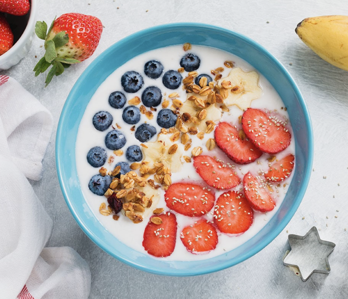 A blue bowl topped with fresh blueberries, strawberries, and star shaped banana slices.