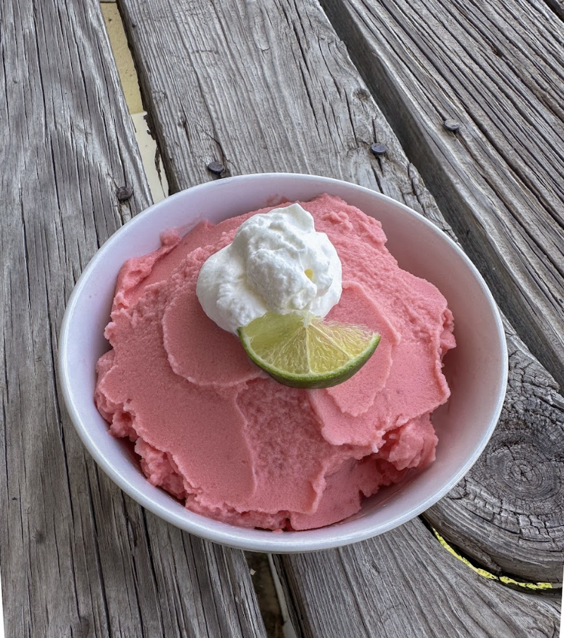 Frozen watermelon sorbet piled into a white bowl and topped with whipped cream.
