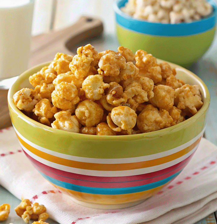 A vibrant bowl of Susan’s Crispy Caramel Corn, filled with golden, glossy caramel-coated popcorn, served in a colorful ceramic bowl on a rustic wooden table