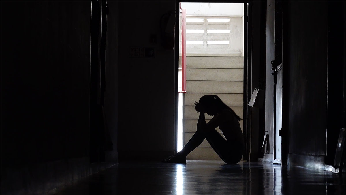 Silhouette of teenage girl sitting on the floor in a doorway in front of stairs with her head in her hands