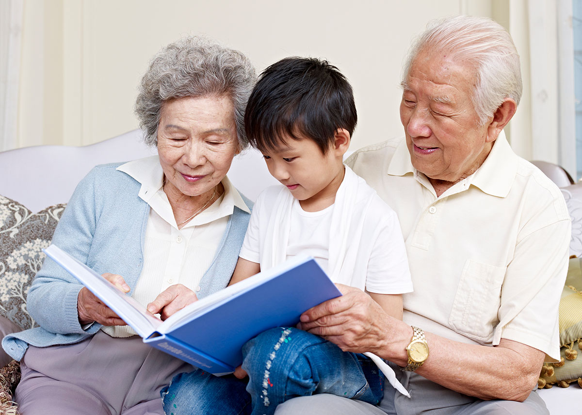 Grandmother and grandfather sitting on a sofa with their grandson, sharing stories and looking at a family photo book