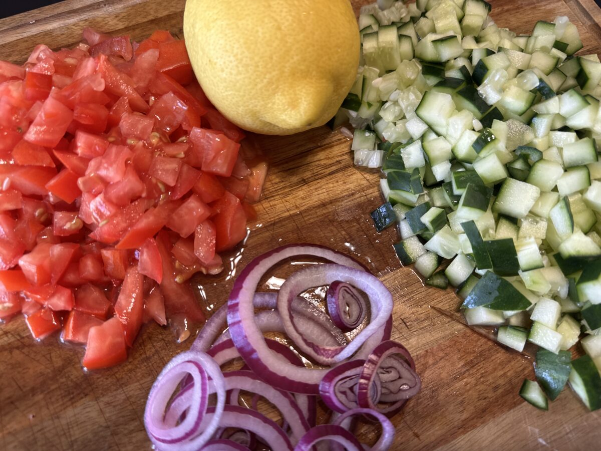 Red onions, tomatoes, cucumbers and a lemon on a cutting board. 