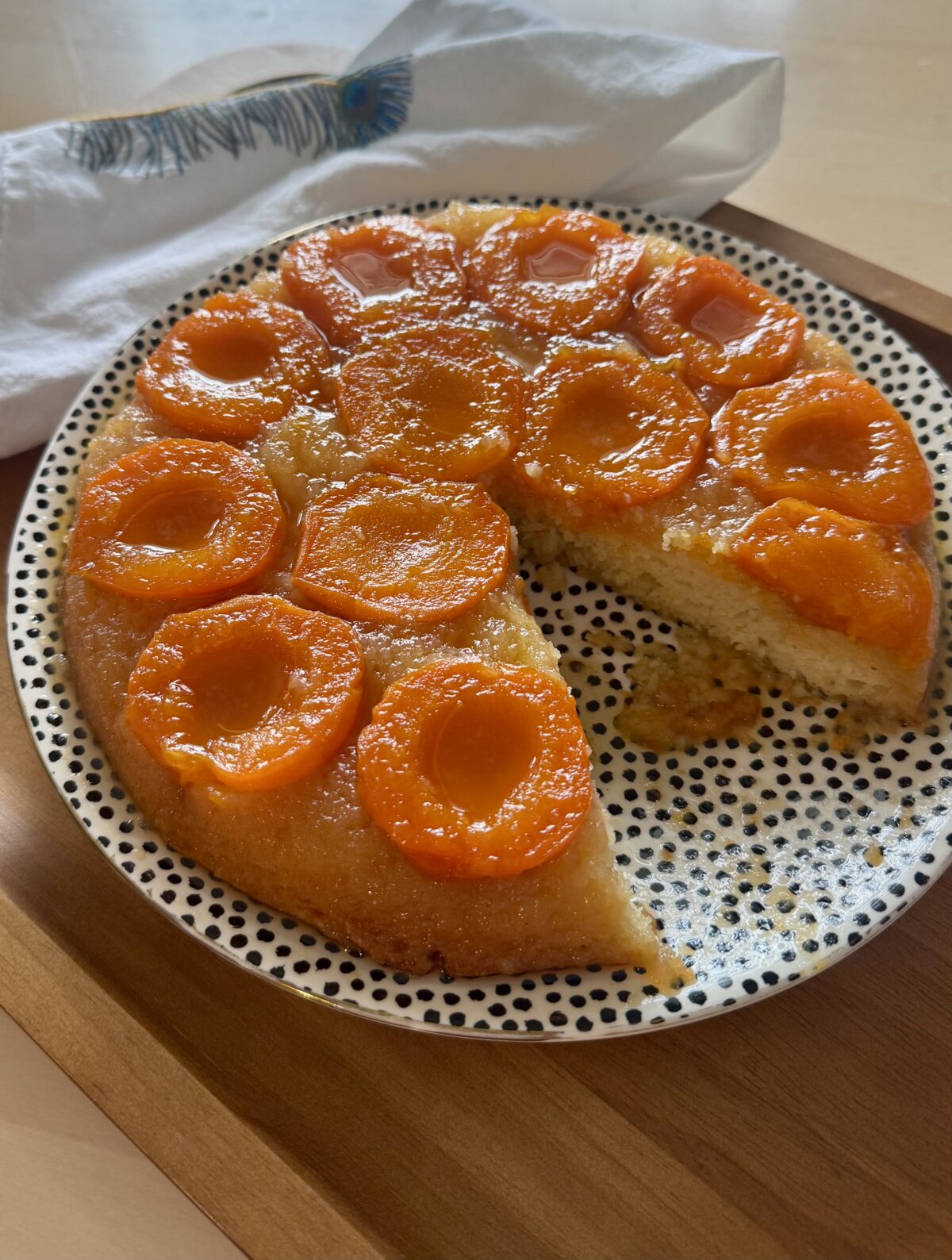 A tart topped with caramelized apricots on a serving plate with a slice removed.